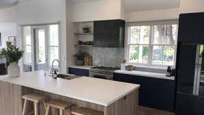 Cocina moderna con una isla grande, armarios oscuros y vistas al exterior a través de amplios ventanales.