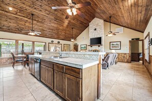 A spacious kitchen with wooden cabinets, a large island, and a stone fireplace. There are ceiling fans, a television, and a dining area visible. - Private pool, pickleball court, single story home, less than 5-minute drive to THE Frio River (Concan)