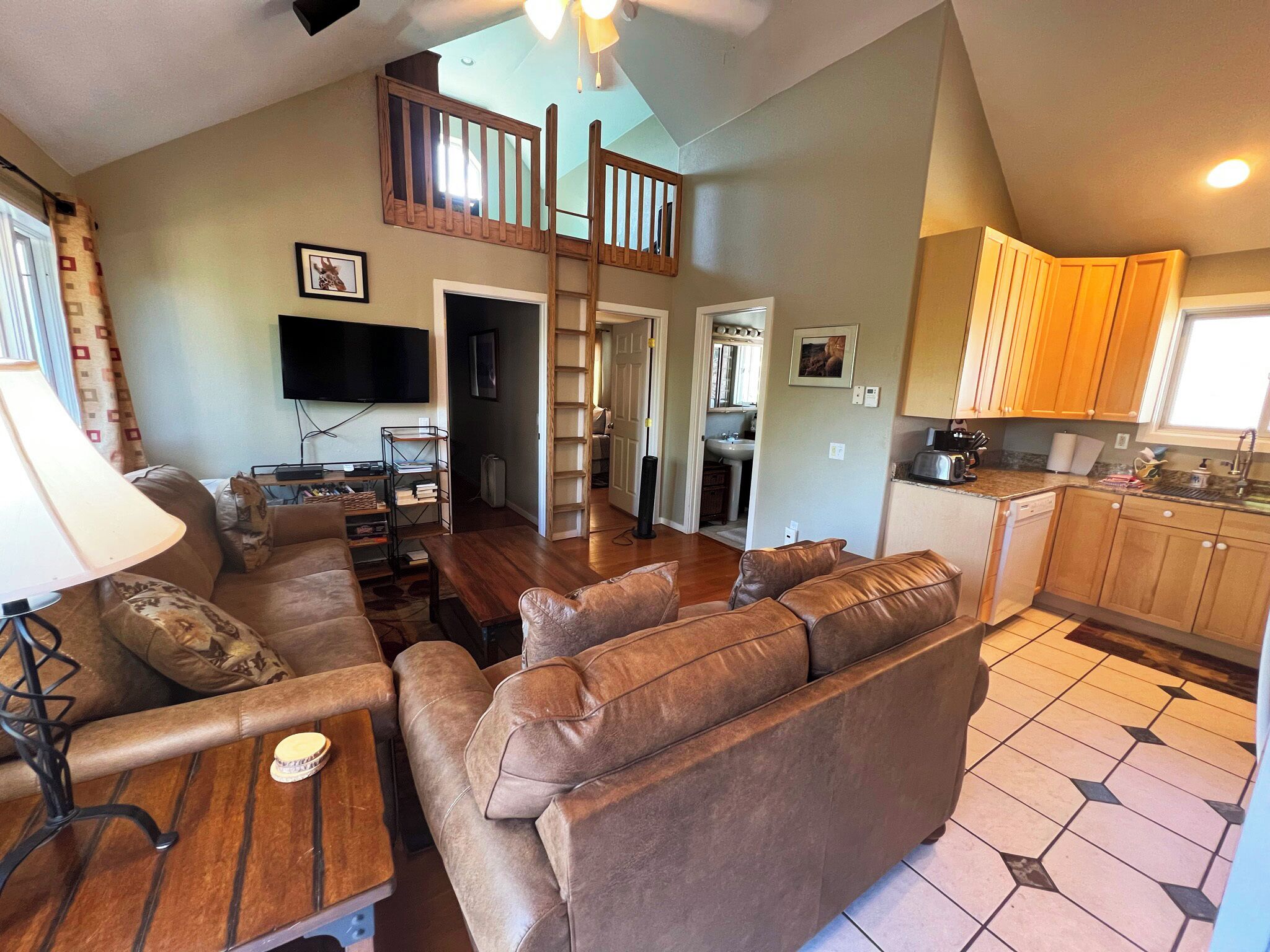 A spacious living room with a leather sofa, a wooden coffee table, and a TV mounted on the wall. A staircase leads to an upper level.