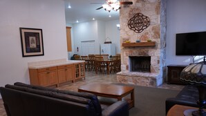 A living room with a fireplace, a dining area with wooden chairs, and a kitchen with wooden cabinets. - Country-style Oasis! The perfect family get-away. VIEW OUR VIDEO!  (San Antonio)
