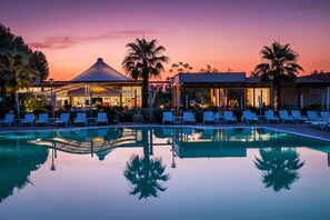 Un espace aménagé au bord de la piscine, avec des chaises longues, et un bâtiment surmonté d’un dôme.