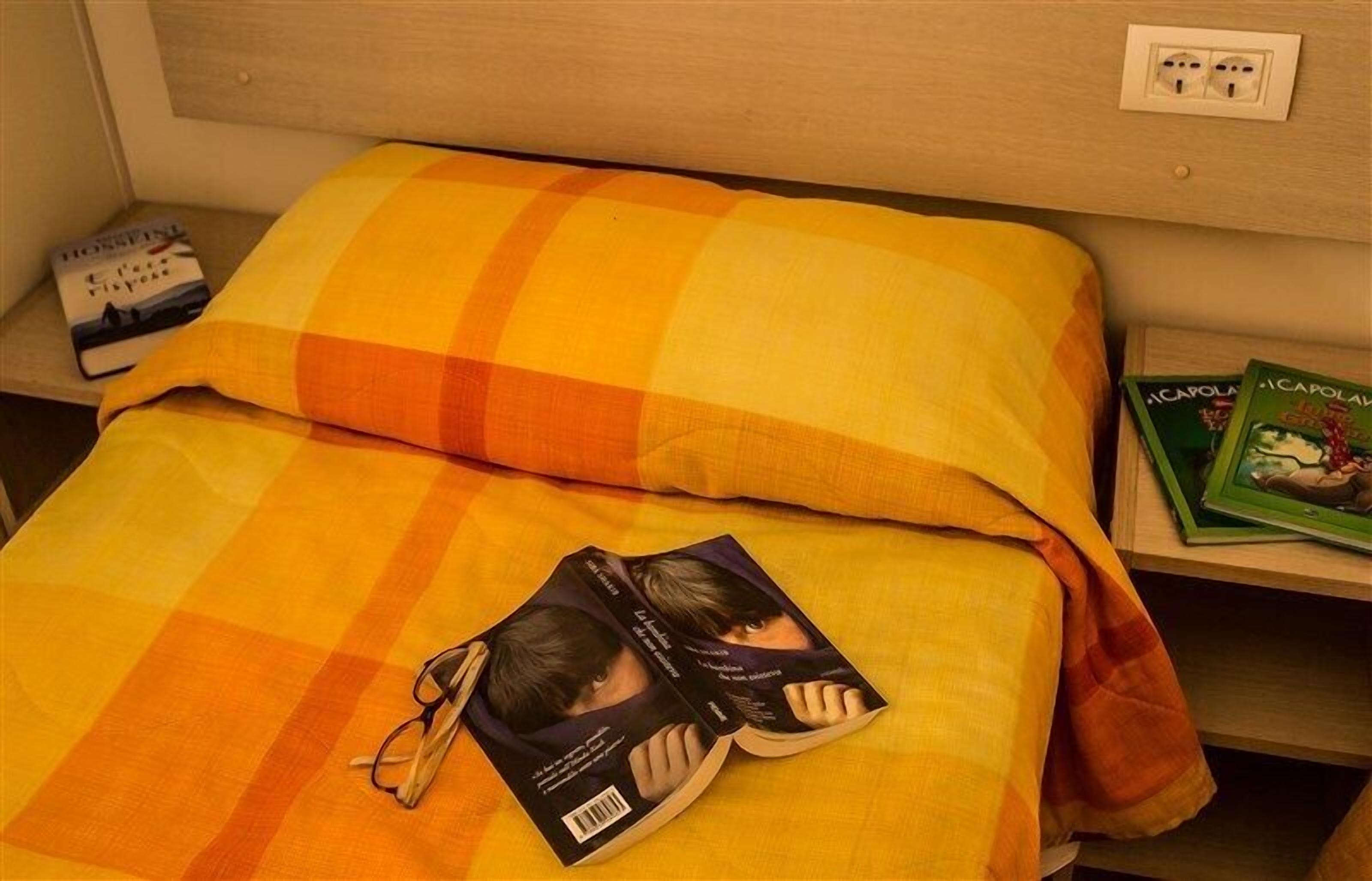 A bed with a checkered blanket and pillows, a book, and a pair of glasses on the bed.