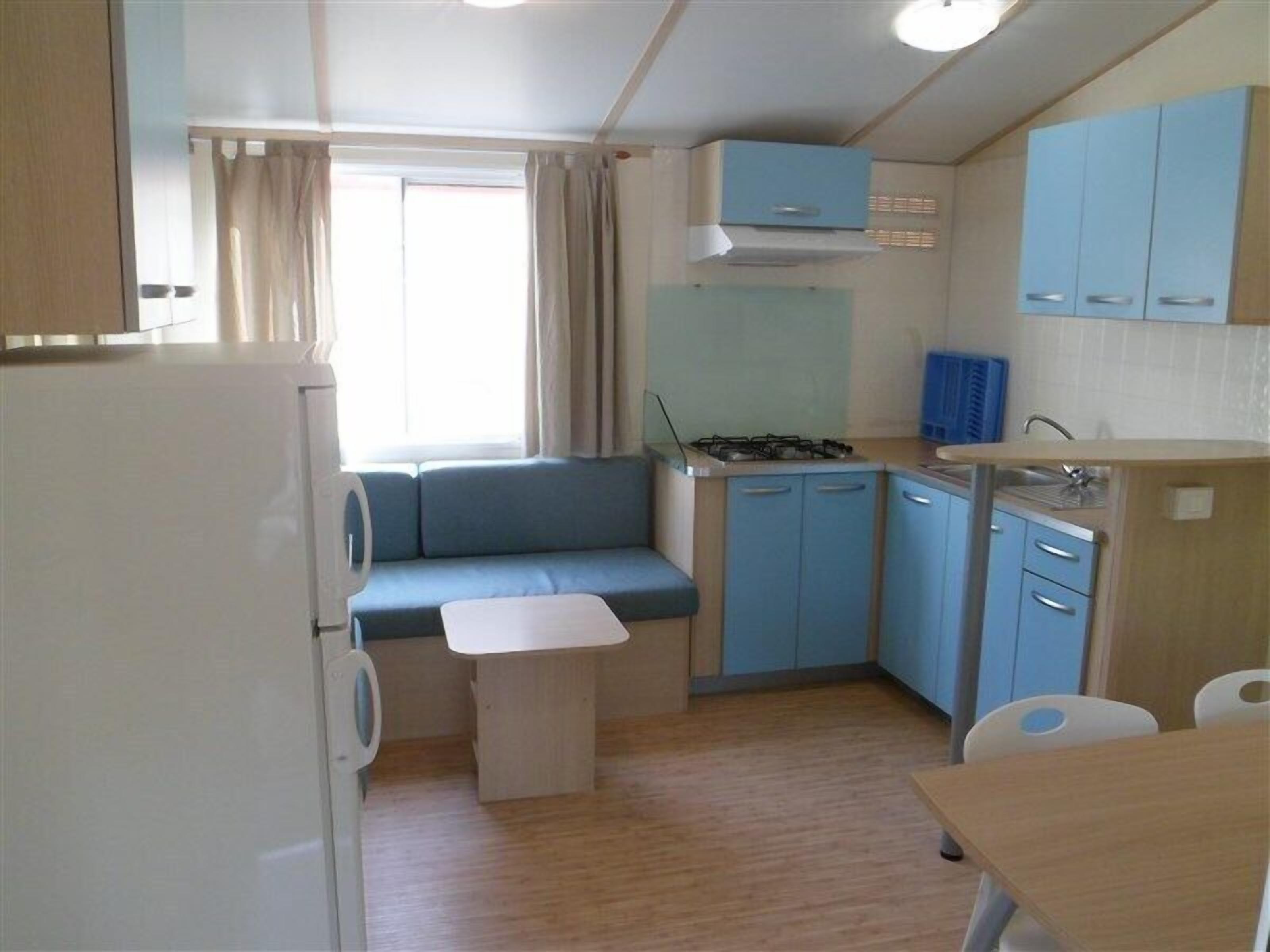 A compact kitchen with a stove, blue cabinets, a small dining table, and a window with curtains.
