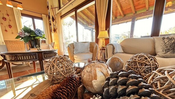 Una sala de estar acogedora con muebles de mimbre, una mesa de centro de vidrio y vistas al exterior a través de ventanas amplias.