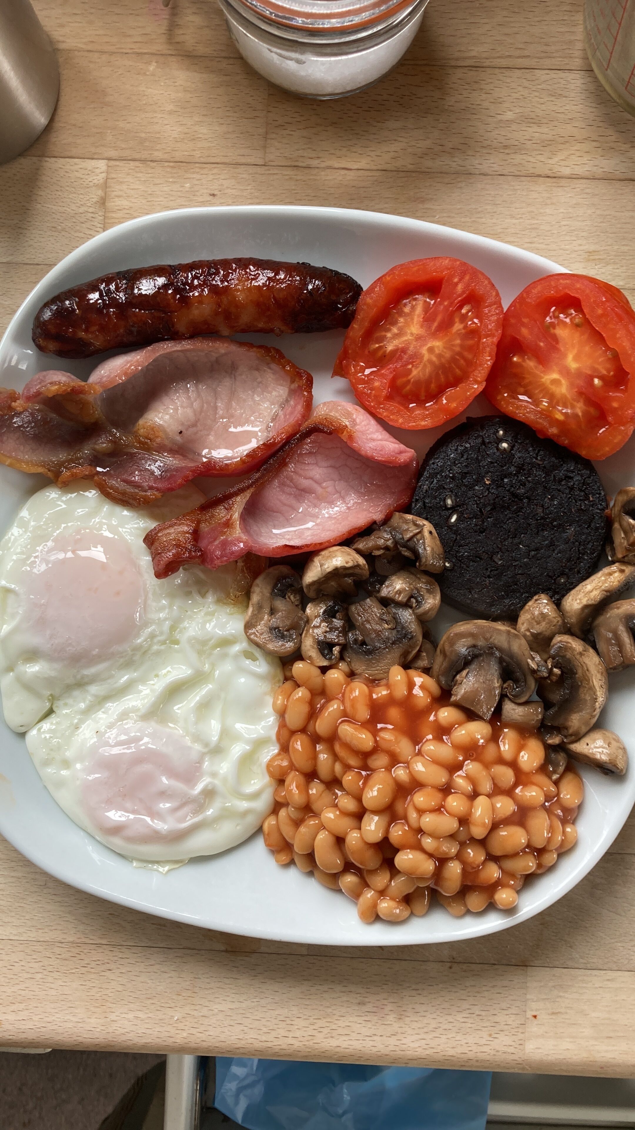 A plate of breakfast food including sausages, bacon, eggs, tomatoes, mushrooms, and baked beans.