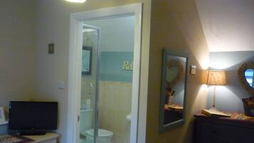 A bathroom with a shower, toilet, and a vanity with a mirror and lamp.