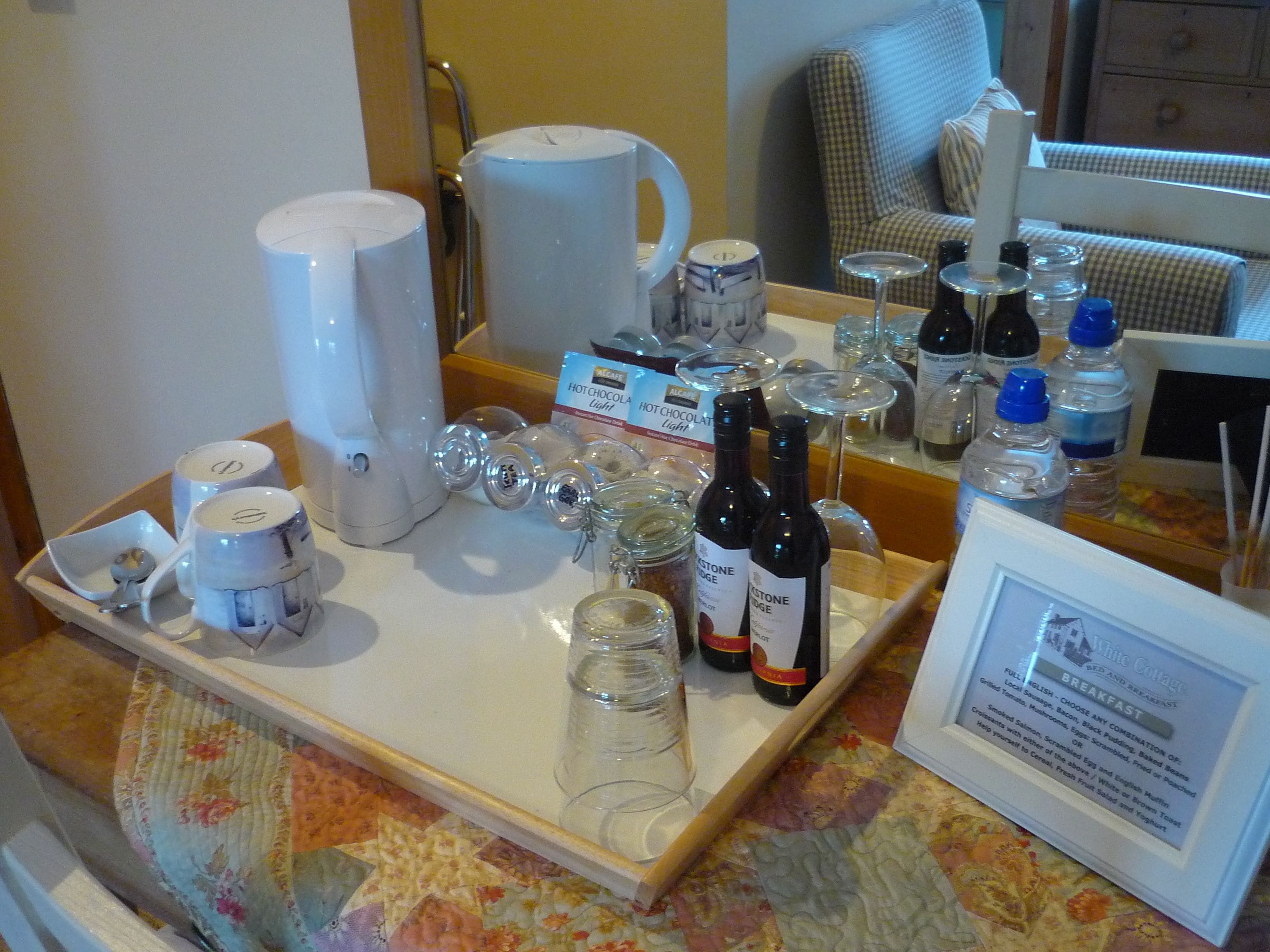 A breakfast tray with hot chocolate mugs, wine glasses, and bottles of wine.