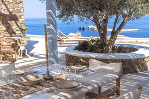 Un espace de restauration en plein air, avec des murs en pierre, une table dressée avec des assiettes, des verres et des couverts, et une vue sur la mer.