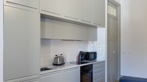 Een compacte keuken met witte kastjes, een roestvrijstalen spoelbak, een zwart fornuis en een magnetron.