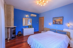 Een slaapkamer met een groot bed, een dressoir, een spiegel, een schilderij en een open haard.