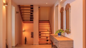 Eine Treppe mit Holzbodenstufen führt zu einer oberen Etage, an der Wand hängt ein Spiegel und ein kleiner Tisch mit einer Pflanze steht daneben.