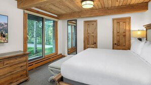 Een slaapkamer met een groot bed, houten balken in het plafond, een houten dressoir en een schuifdeur naar een balkon.