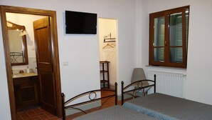 A bedroom with a bed, a wooden door, a mirror, a TV, and a window with blinds. - From the Piero hill you can admire the Valtiberina where Tuscany and Umbria merge (Sansepolcro AR)
