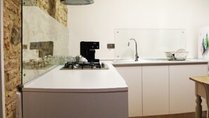 A compact kitchen with a gas stove, sink, and white cabinets. There is a dining table with chairs, a sofa, and a fireplace. - From the Piero hill you can admire the Valtiberina where Tuscany and Umbria merge (Sansepolcro AR)