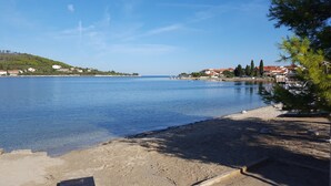 A coastal view with a sandy beach, calm water, and houses in the background.