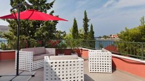A terrace with white wicker furniture, a red umbrella, and potted plants.