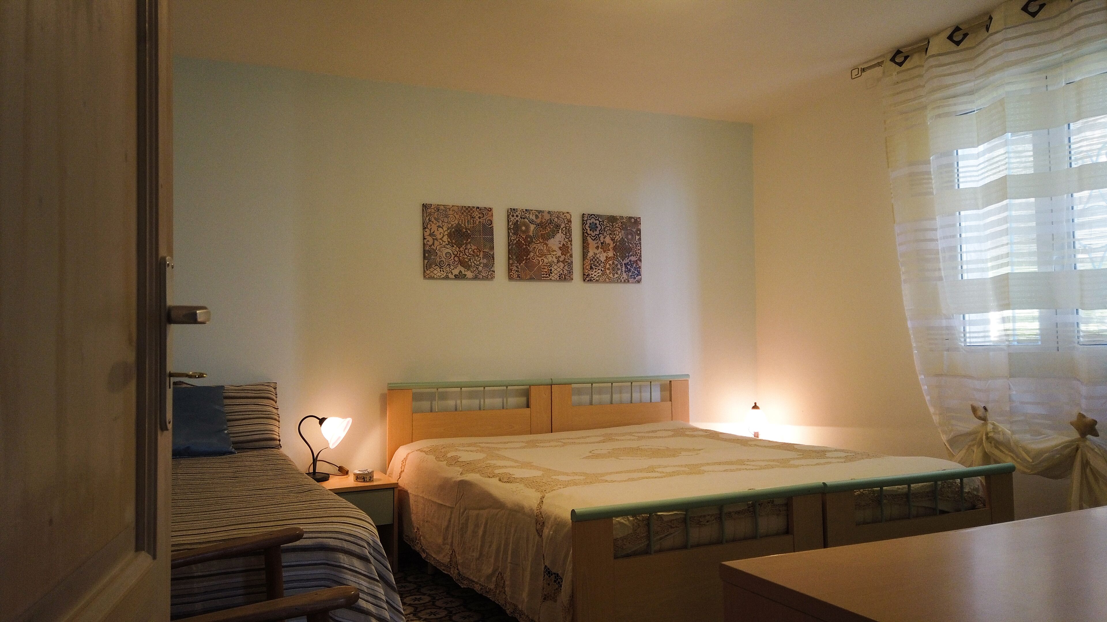 A bedroom with a bed, bedside tables, a nightstand, a chair, and a window with curtains.