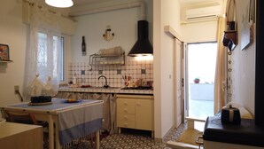 Une cuisine compacte comprenant une table à manger, une cuisinière et un évier. On y trouve une fenêtre avec des rideaux, une plante en pot et une petite table avec une tasse.