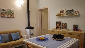 Un salon chaleureux avec un canapé, une table sur laquelle sont disposés des fruits et des tasses, un poêle et des objets décoratifs sur des étagères.