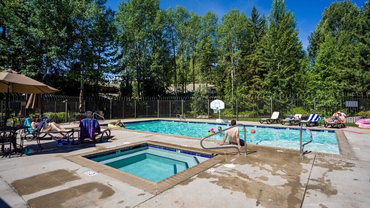 A swimming pool area with multiple pools, lounge chairs, and a basketball hoop.