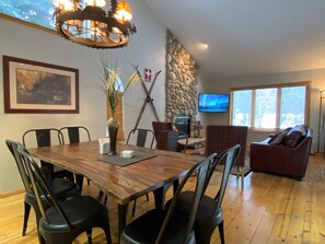 Zona pranzo con tavolo e sedie in legno, parete in pietra, camino e televisore.