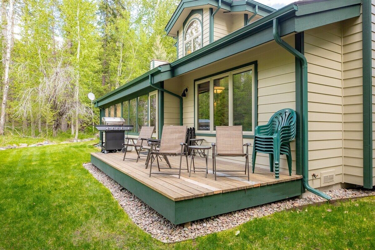 Une terrasse couverte, aménagée avec du mobilier d’extérieur, un barbecue et offrant une vue sur une zone boisée.