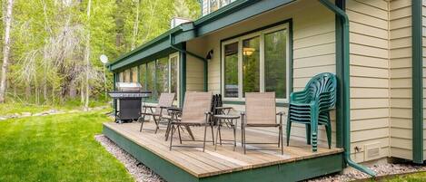Une terrasse couverte, aménagée avec du mobilier d’extérieur, un barbecue et offrant une vue sur une zone boisée.