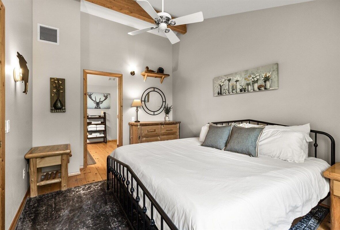 A bedroom with a bed, a ceiling fan, a wooden dresser, a mirror, and a wall-mounted shelf with decorative items.
