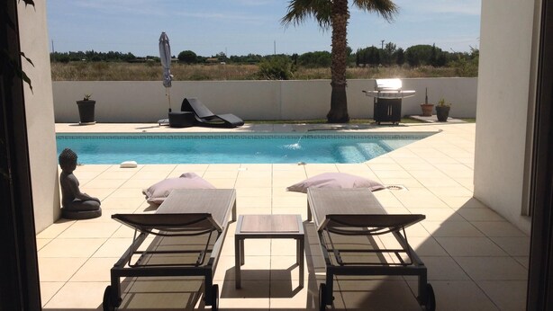 Un espace aménagé au bord de la piscine, avec des chaises longues et une statue, ainsi qu’un barbecue et une vue sur le paysage.