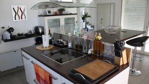 Une cuisine moderne dotée d’un îlot central, d’une cuisinière à façade en verre, ainsi que de divers appareils de cuisine et ustensiles.