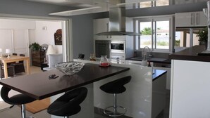 Une cuisine moderne dotée d’un îlot central, de tabourets de bar, d’une grande fenêtre et d’un coin repas avec une table et des chaises.