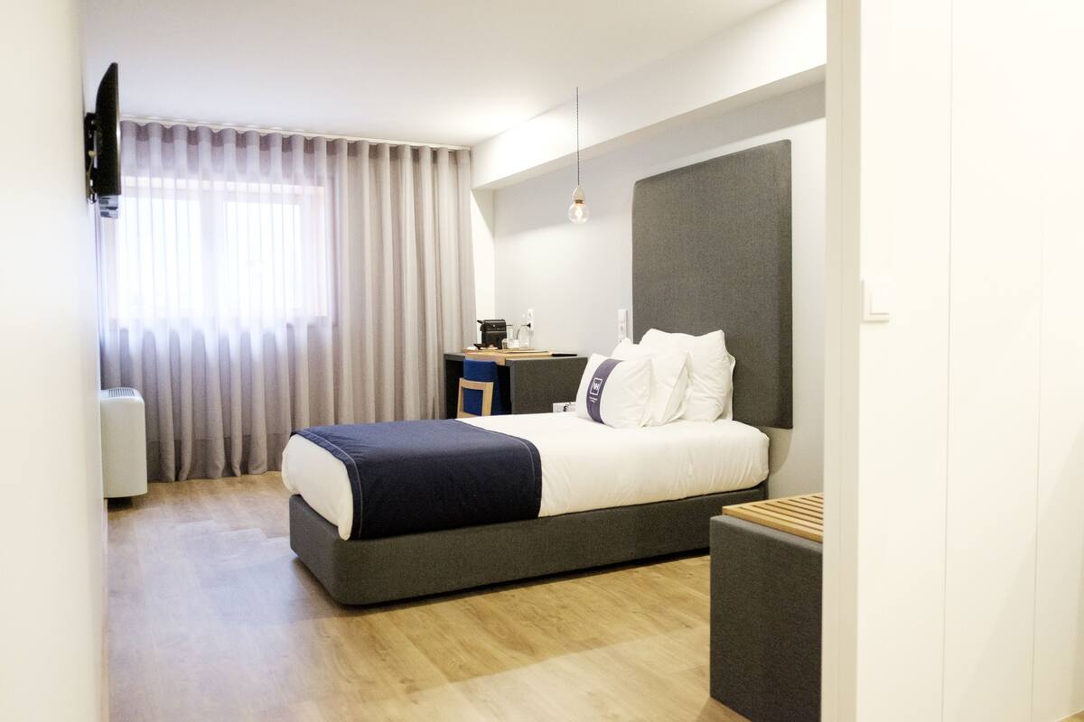 Une chambre d’hôtel moderne, dotée d’un grand lit, d’un bureau et d’un téléviseur fixé au mur.