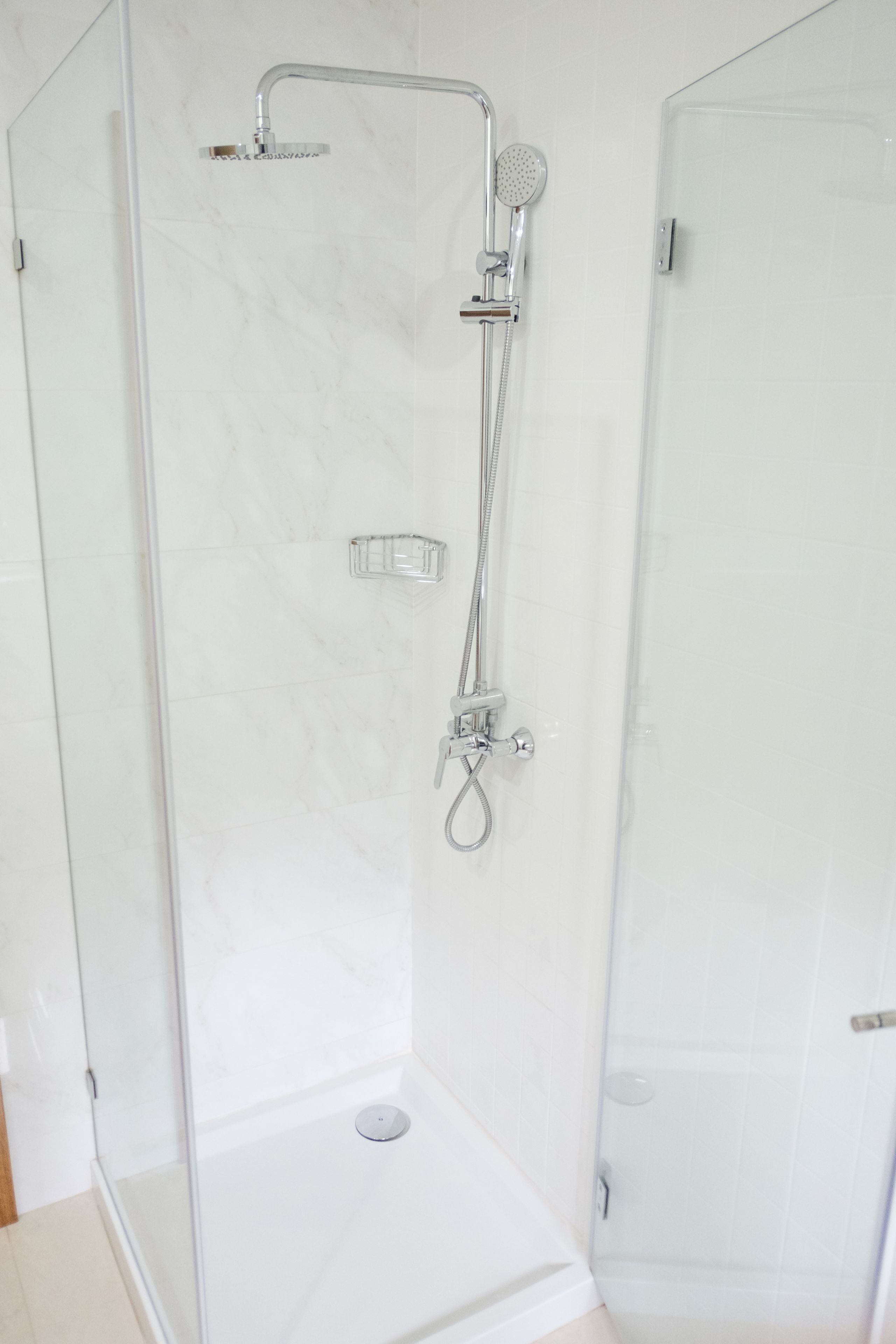 A glass-enclosed shower stall with a handheld showerhead and a handheld shower attachment.