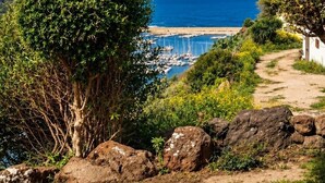 A coastal landscape with a clear sky, a pathway leading to a beach, and boats docked in the water. - Luxury apartment with stunning sea views and close to sea and shops, WI-FI,clima (Castelsardo)