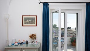 A room with a glass door leading to an outdoor area, a framed picture on the wall, and a small table with various items. - La Ninfa Di Capri (Anacapri)
