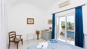 A hotel room with a bed, a chair, a small cabinet, a window with curtains, and a view of the outdoors. - La Ninfa Di Capri (Anacapri)