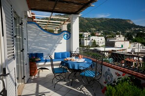 A balcony with a table set for two, a blue sofa, and a potted plant. - La Ninfa Di Capri (Anacapri)
