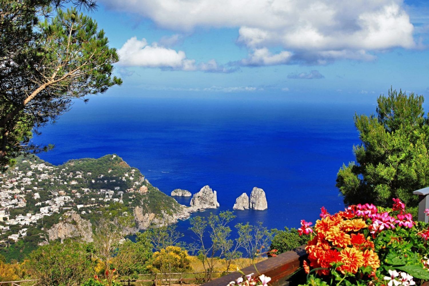A coastal landscape with a view of the sea, rocky formations, and a town on a hillside.