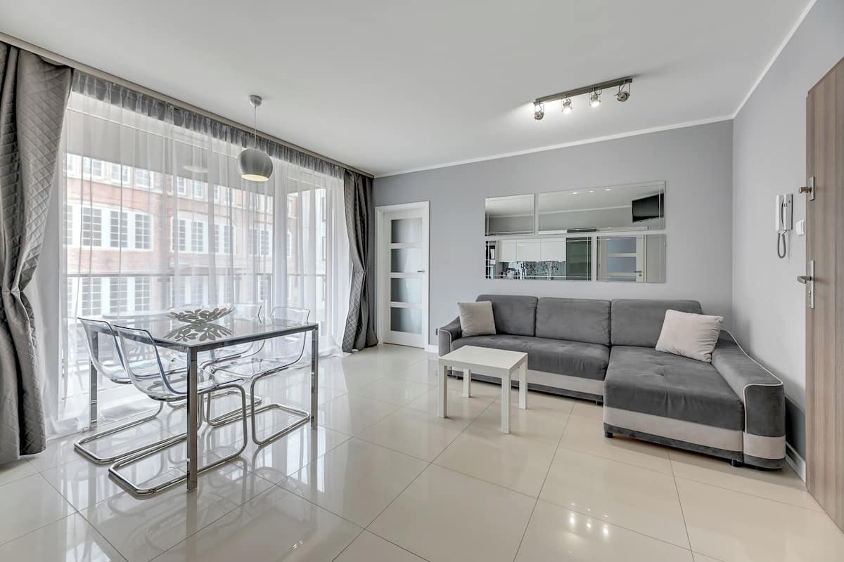 A modern living room with a glass dining table, a grey sofa, and a white coffee table.