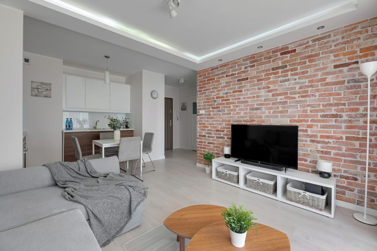 A modern living room with a grey sofa, a wooden coffee table, and a brick accent wall.