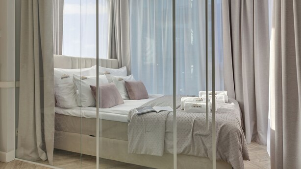 Una habitación de hotel moderna con una cama grande, una mesita de noche y vistas a través de cortinas de gasa.