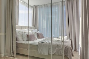 A modern hotel room with a large bed, a bedside table, and a view through sheer curtains. - Chmielna Park by Downtown Apartments (Gdansk)