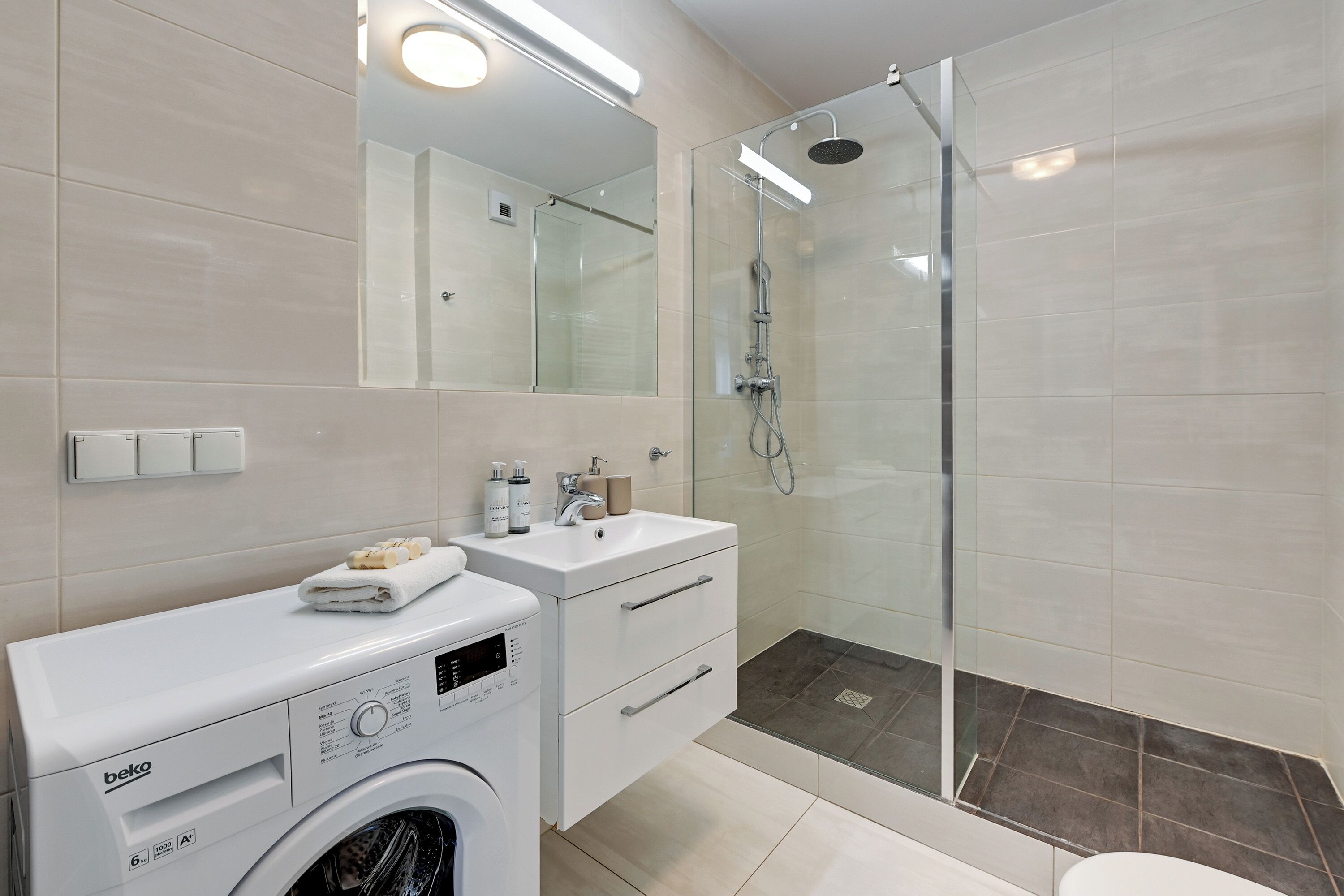 A modern bathroom with a washing machine, a sink, and a glass-enclosed shower.