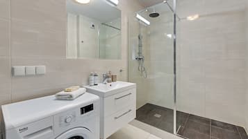 A modern bathroom with a washing machine, a sink, and a glass-enclosed shower.