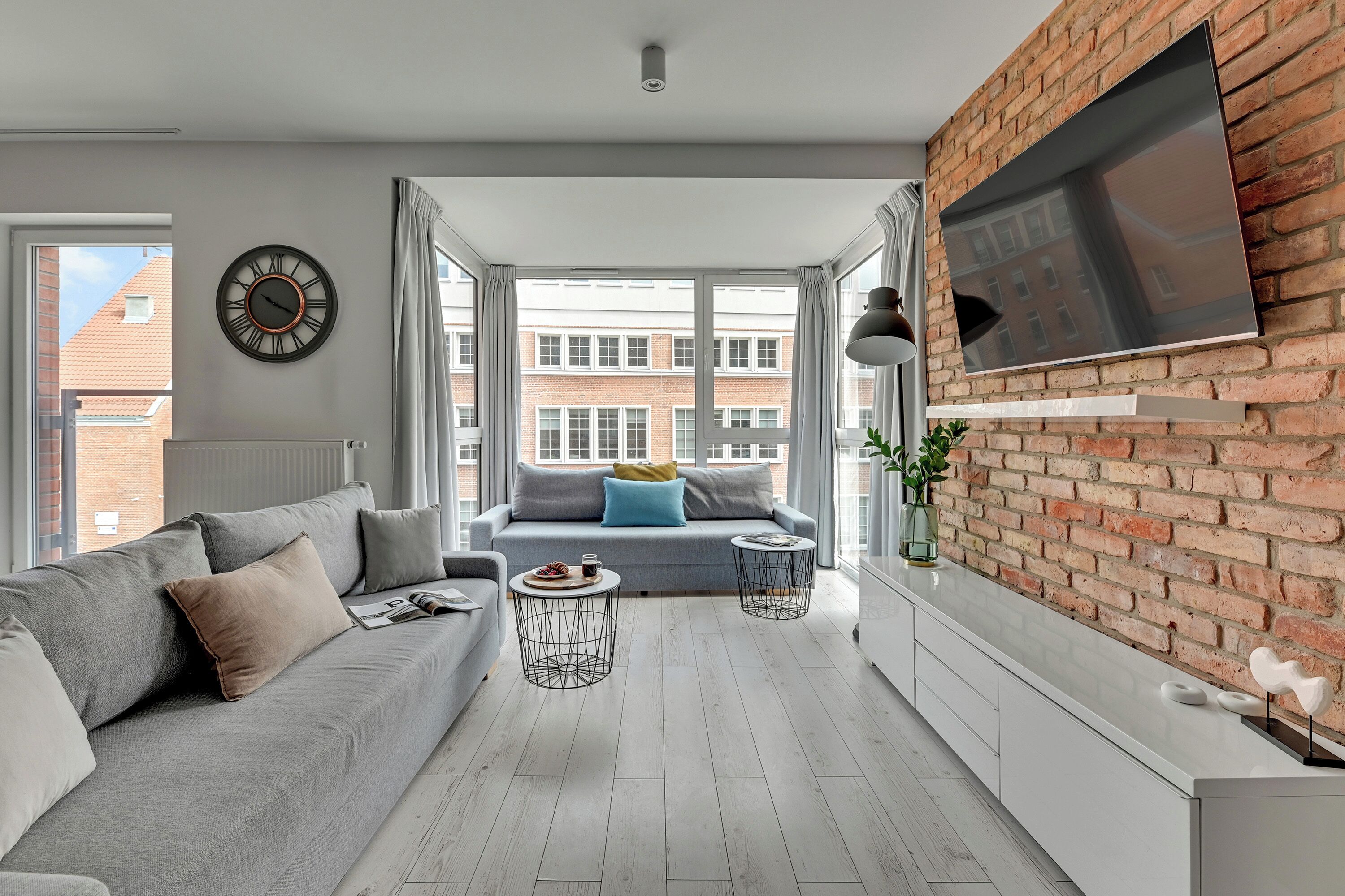 Un salon moderne avec un canapé gris, une table basse et un téléviseur fixé au mur, qui est en briques.