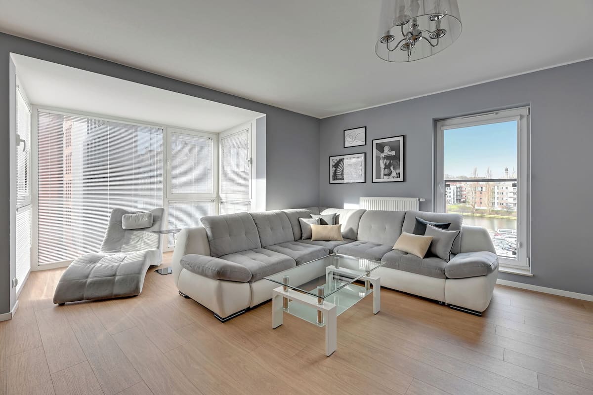 A modern living room with a sectional sofa, a glass coffee table, and large windows offering a view of the city.