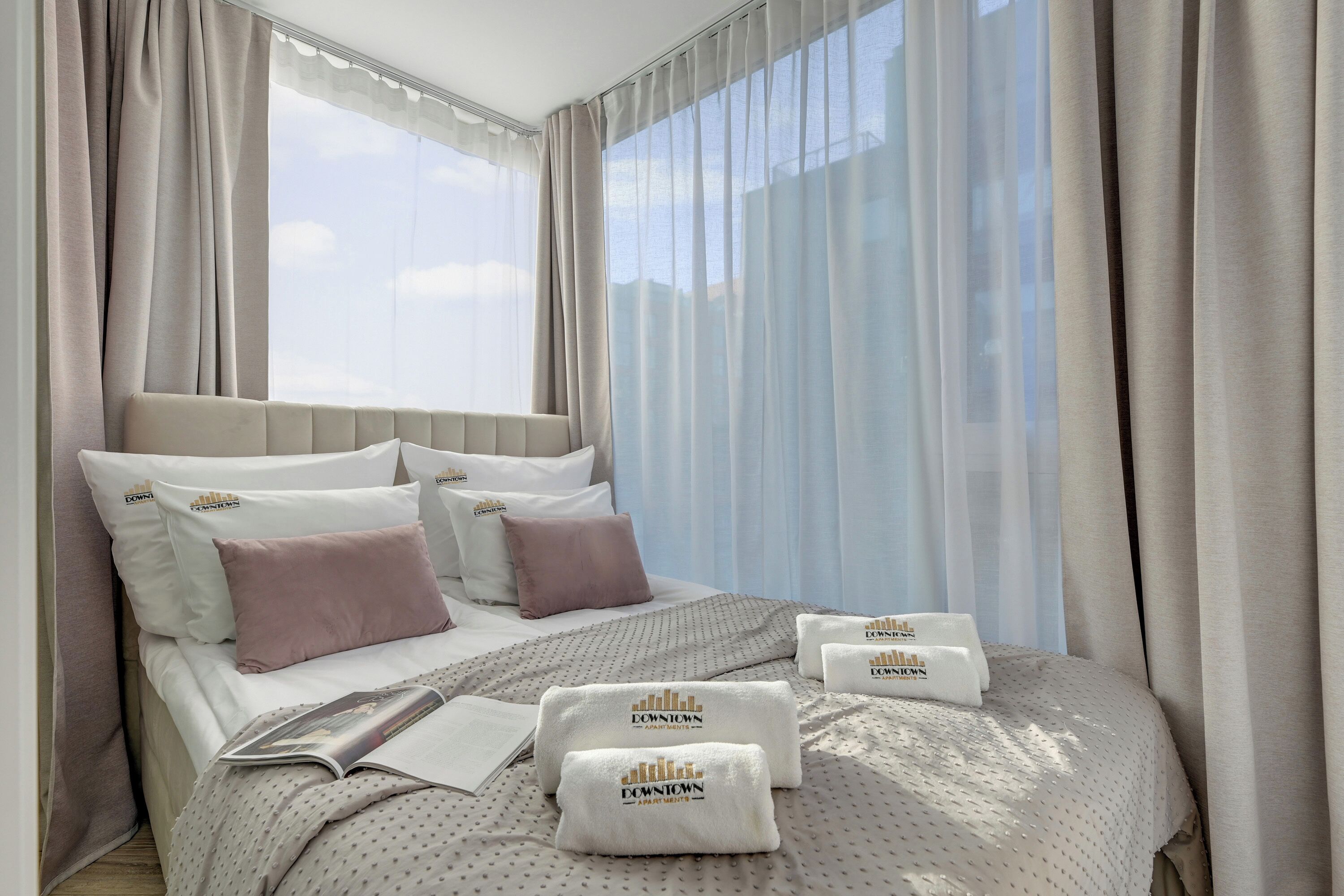 A hotel room with a large bed, multiple pillows, a blanket, and a magazine.
