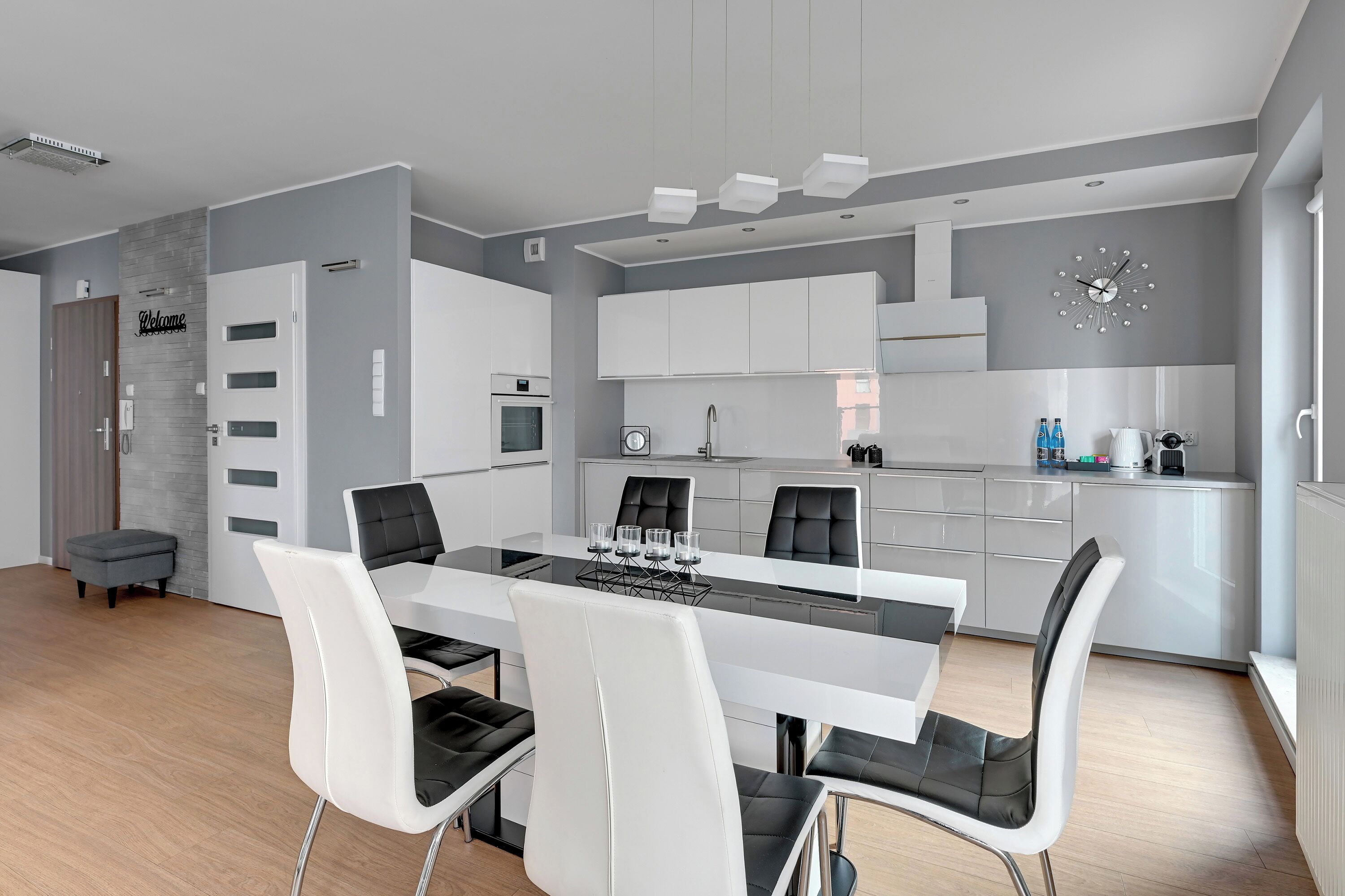 A modern kitchen with white cabinets, a central island, and a dining area with white chairs and a glass table.