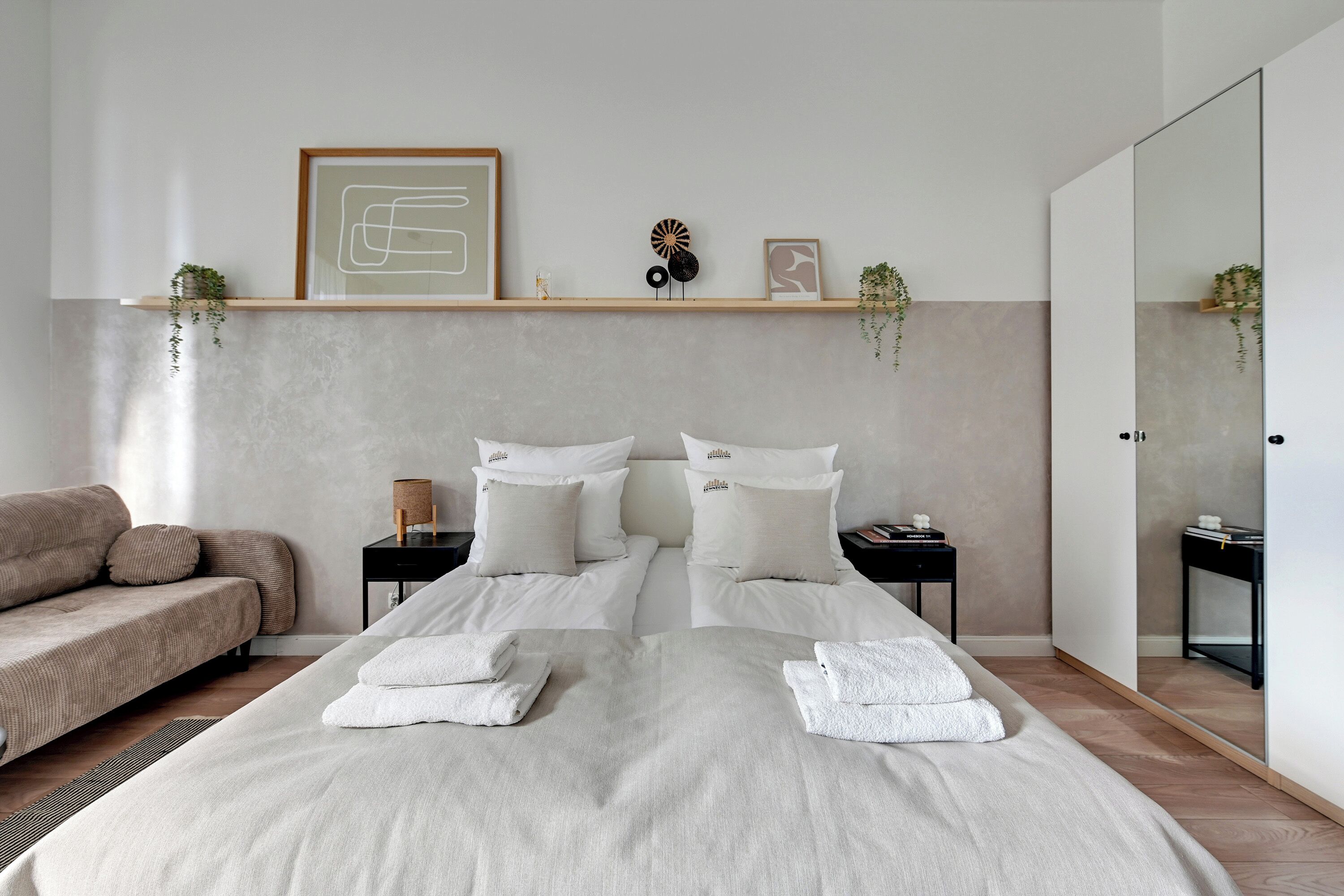 A modern bedroom with a large bed, two bedside tables, a sofa, and a mirror.