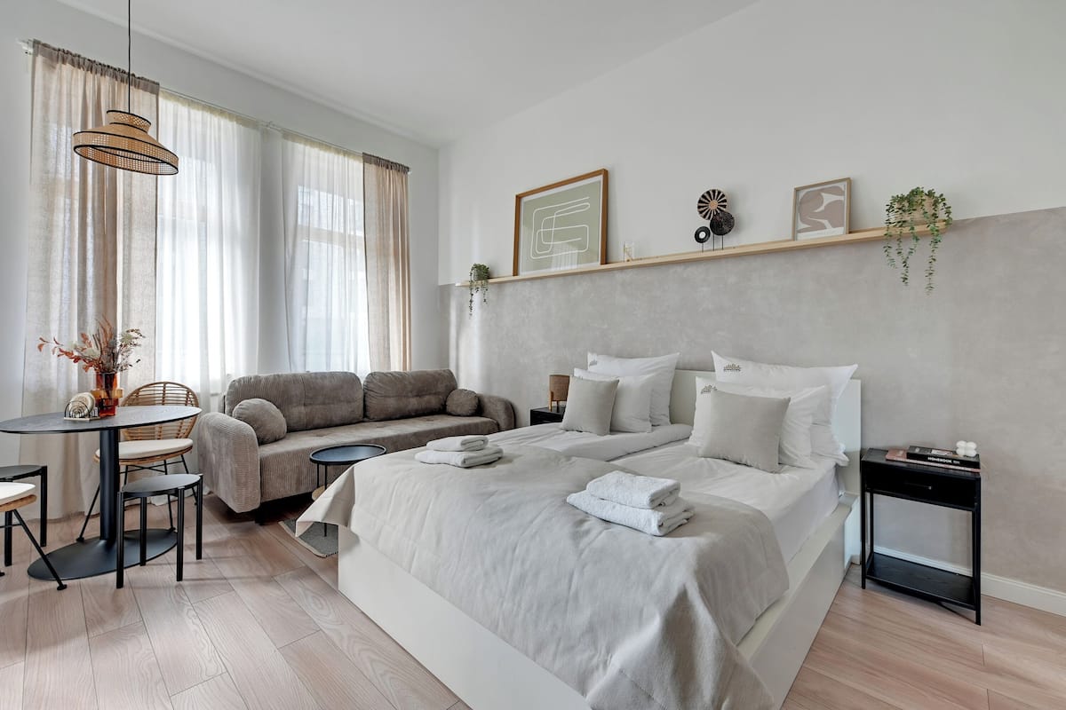 A modern bedroom with a large bed, a sofa, a dining table, and a small side table.
